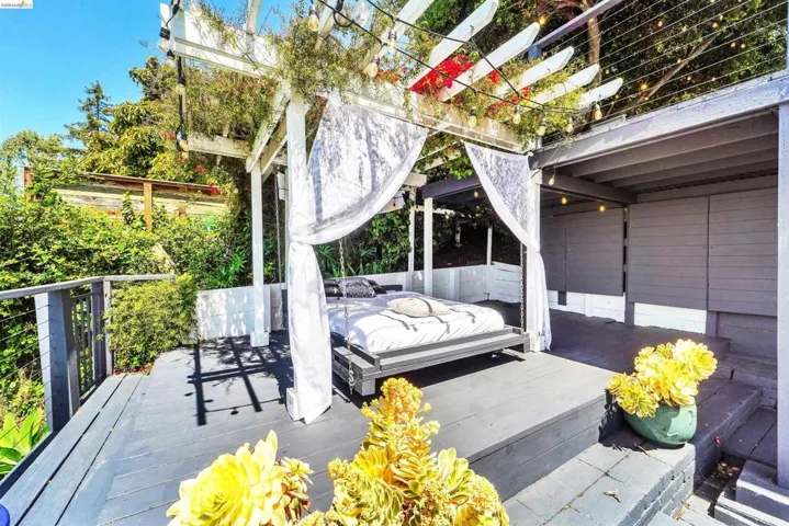 Outdoor wooden deck featuring a white pergola with string lights, lush surrounding greenery, and a cable railing system