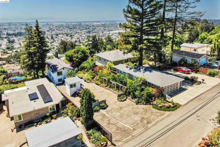 Hillside property featuring a multi-level structure with a two-car garage, mature trees, and a paved driveway