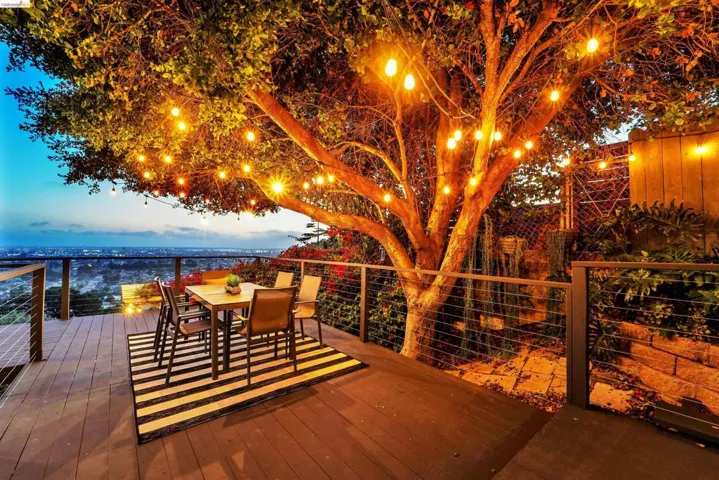 Expansive outdoor deck featuring composite decking, cable railing, and a mature tree adorned with string lights