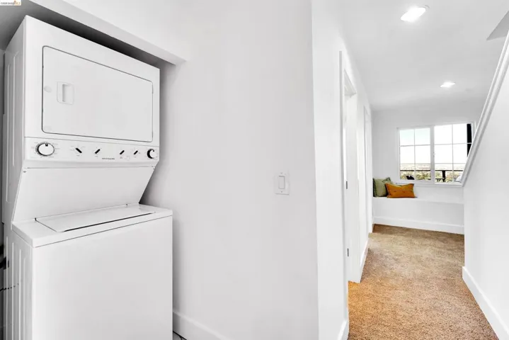 Integrated laundry center with a stacked washer and dryer, adjacent to a hallway with a built-in window bench and white trim