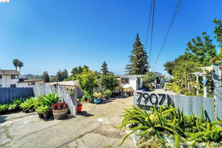 Property entrance featuring a gray picket fence, integrated house numbers, and a variety of mature plantings