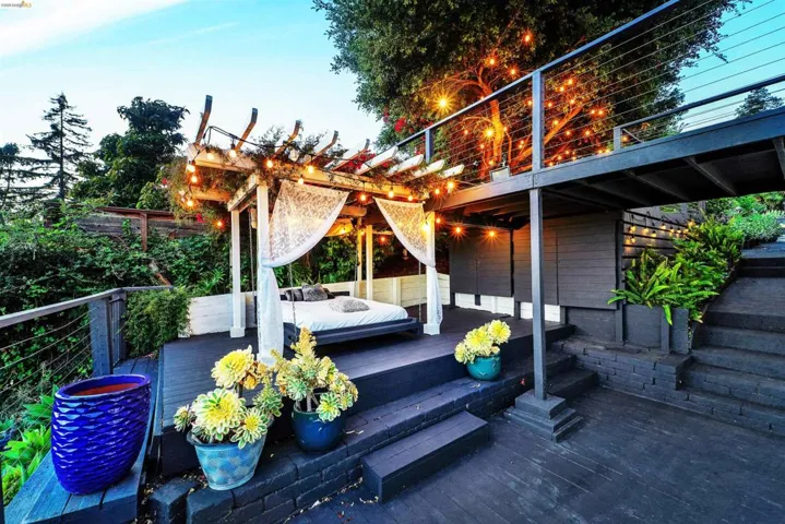 Multi-level exterior decking featuring an open pergola with string lighting, cable railing, and integrated planter boxes