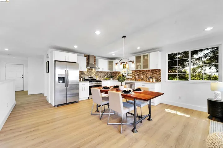 Open-concept living area featuring a modern kitchen with stainless steel appliances, light wood-finish flooring, white cabinetry, a tiled backsplash, and recessed lighting
