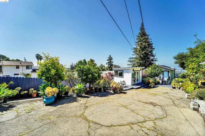 Outdoor space featuring a cracked paved surface, a blue picket fence, and multiple potted plants