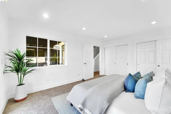 Carpeted room featuring a large window with white muntins, recessed lighting, and two sliding closet doors