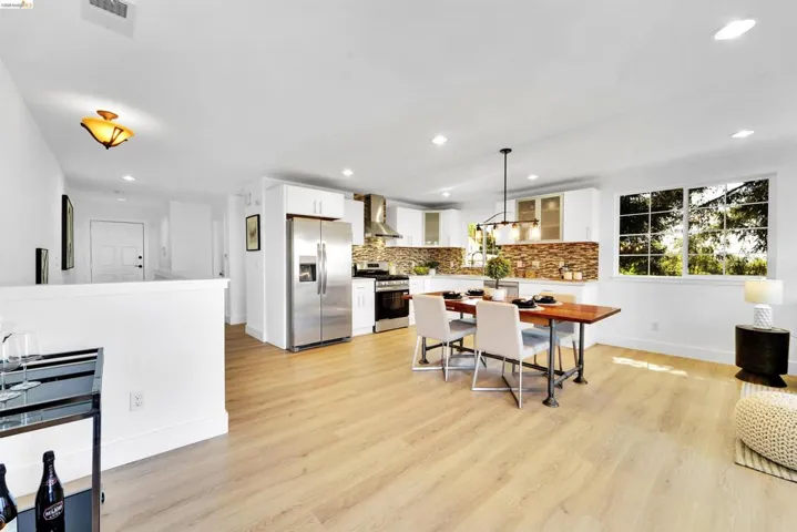 Open-concept living space featuring wood-finish flooring, recessed lighting, and a kitchen with stainless steel appliances, white cabinetry, and a stone-tile backsplash