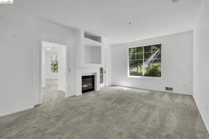 Living space featuring a fireplace with built-in shelving, a large window, light gray carpeting, and neutral white walls