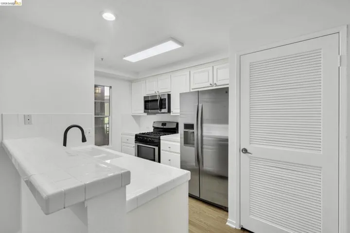 Kitchen featuring white tiled countertops and backsplash, stainless steel appliances, white cabinetry, and wood-finish flooring