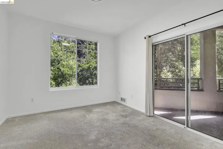 Carpeted interior space featuring a large window, recessed lighting, and a glass sliding door opening to an outdoor balcony with metal railings and a concrete surface