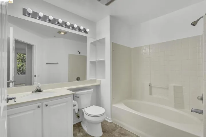 Bathroom featuring a white vanity with integrated sink, a large wall-mounted mirror, overhead vanity lighting, a built-in bathtub with shower, and tiled walls