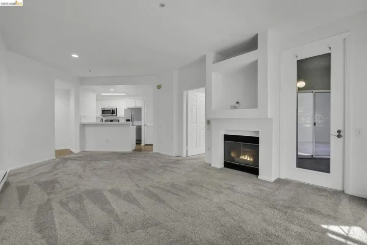 Living area featuring light gray carpeting, a built-in fireplace with a black surround, and integrated shelving