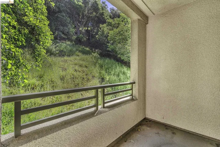 Outdoor balcony with textured stucco walls, dark railing, and concrete flooring