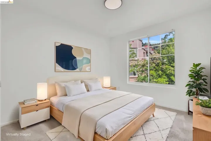 Light-filled bedroom featuring a large window, neutral wall paint, and gray carpet flooring