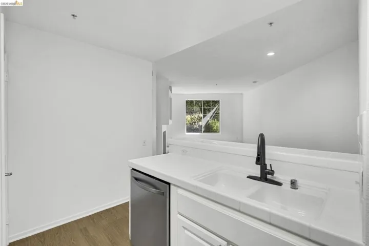 Kitchen area featuring a built-in dishwasher, white tile countertop, integrated sink, and a matte black faucet