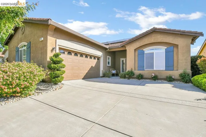 Stucco exterior featuring a two-car garage with arched window inserts, a concrete driveway, and established front landscaping