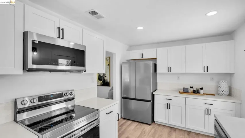 Kitchen featuring white cabinetry with black hardware, stainless steel appliances, light countertops, and wood-finish flooring