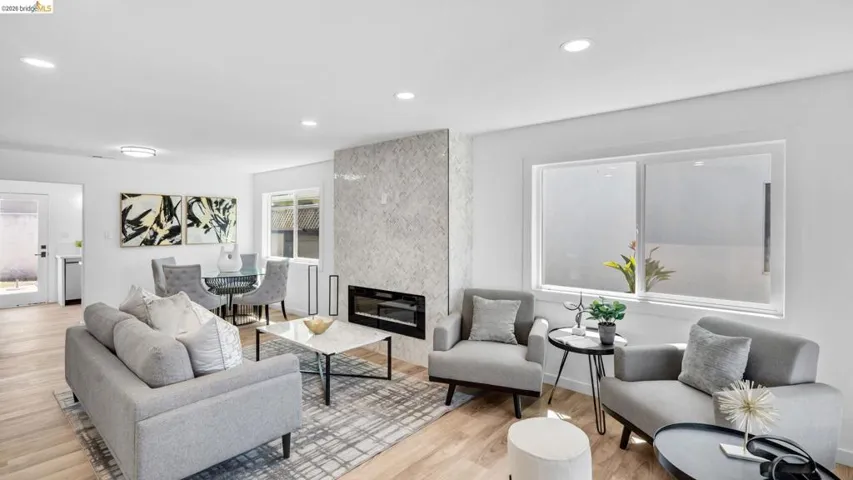 Living space featuring a tiled fireplace surround with an inset linear electric fireplace, wood-finish flooring, recessed lighting, and a large window