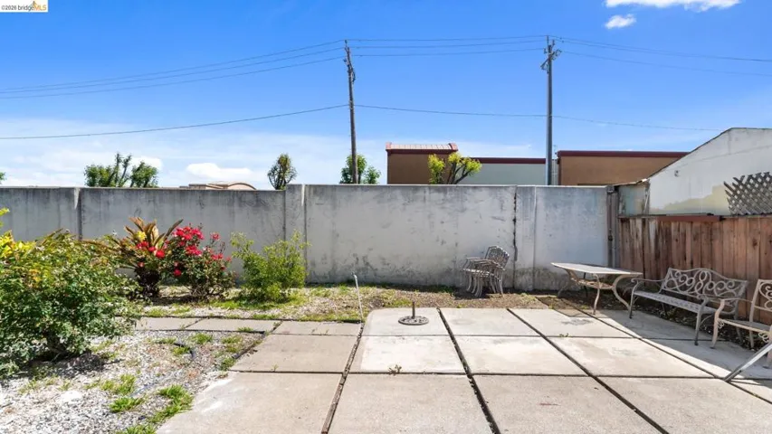 Outdoor patio space featuring large concrete pavers, a partial privacy fence, and planted shrubbery