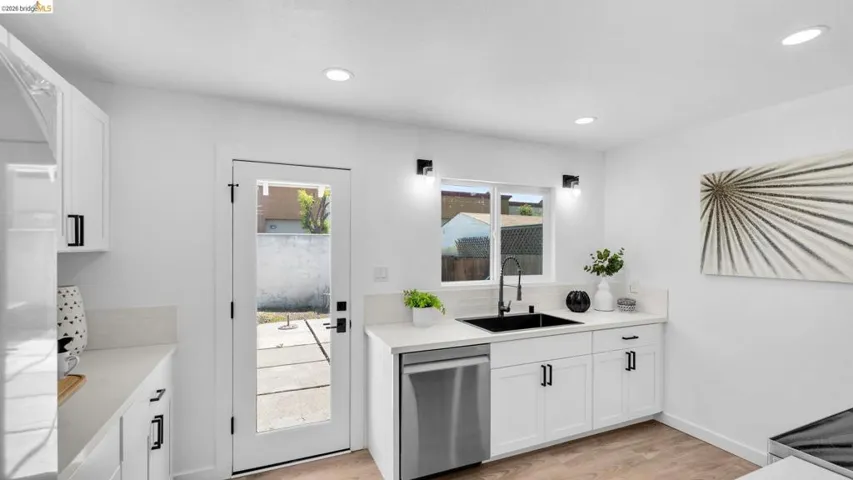 Modern kitchen featuring white cabinetry, light countertops, a black sink, and stainless steel appliances