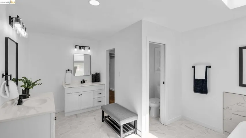 Bright bathroom with dual vanities featuring white cabinetry, light countertops, and black fixtures