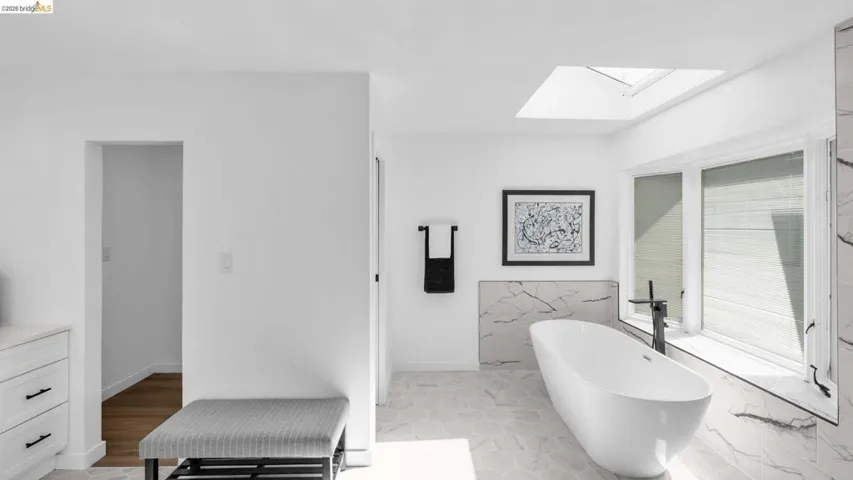 Freestanding soaking tub with a matte black floor-mounted faucet, complemented by a skylight and a large window