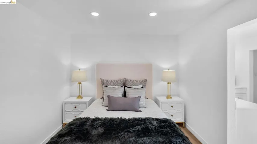 Crisp white walls frame this bedroom with recessed lighting and wood-finish flooring