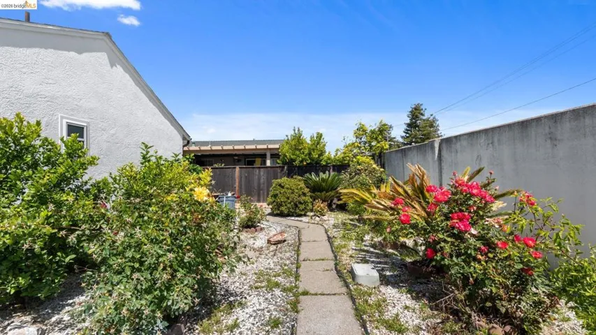 Path of concrete pavers through a garden featuring mature shrubs and vibrant red and yellow roses