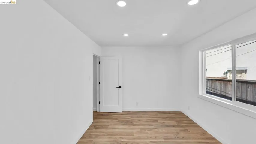 Bright room featuring recessed lighting, wood-finish flooring, a white paneled door with matte black hardware, and a large window with white trim