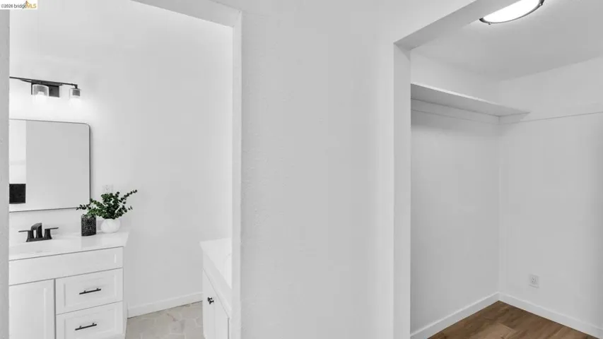 Bathroom vanity with white cabinetry, a single basin sink, and matte black fixtures, complemented by a contemporary wall-mounted mirror and overhead lighting
