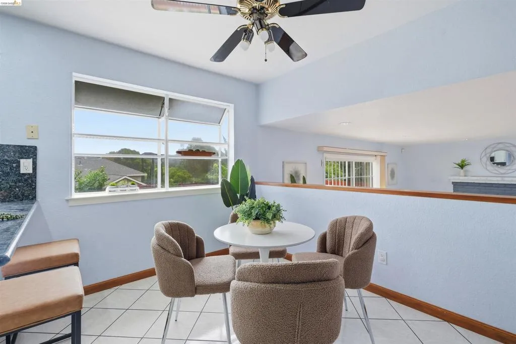 Kitchenette area featuring a large casement window, ceiling fan with integrated lighting, tiled flooring, wood baseboards, and a built-in counter with a dark countertop