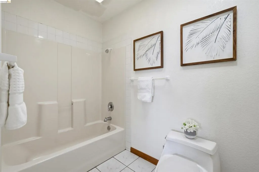 Bathroom featuring a white bathtub with an integrated shower, white tiled flooring, and a white toilet