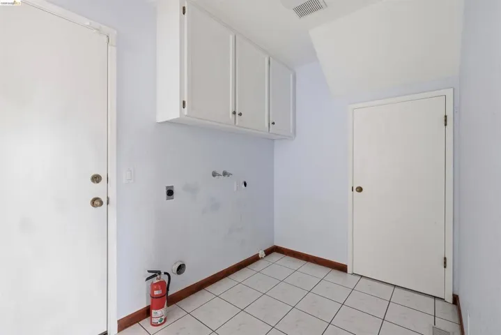 Dedicated utility space featuring white upper cabinetry, tiled flooring, and multiple utility hookups