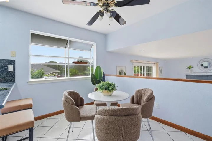 Kitchenette area featuring a large casement window, ceiling fan with integrated lighting, tiled flooring, wood baseboards, and a built-in counter with a dark countertop