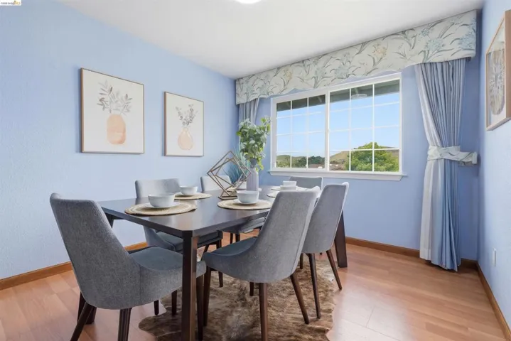 Dining area featuring wood-finish flooring, a large window with white framing, and light blue walls