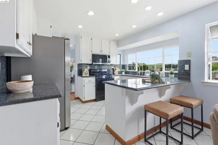 Kitchen featuring white cabinetry, dark stone countertops, stainless steel refrigerator, black range, and built-in breakfast bar