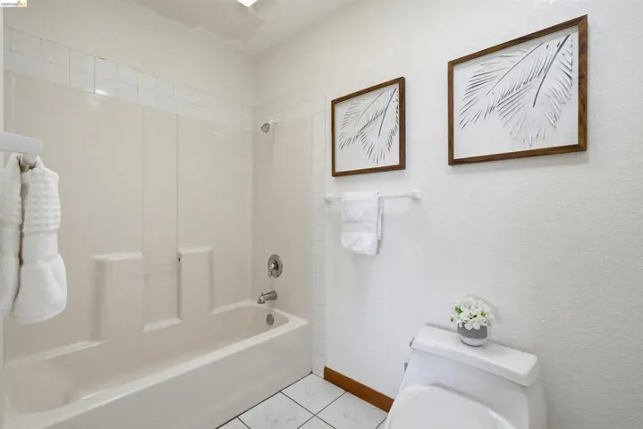Bathroom featuring a white bathtub with an integrated shower, white tiled flooring, and a white toilet