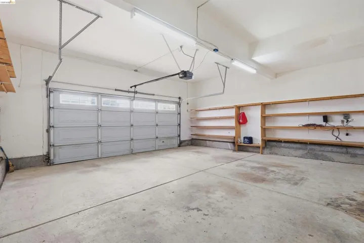 Spacious garage featuring a concrete floor, built-in shelving, white walls, and a sectional garage door with upper-row windows