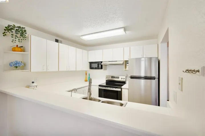 Bright kitchen featuring white cabinetry, light countertops, stainless steel appliances, and a dual basin sink