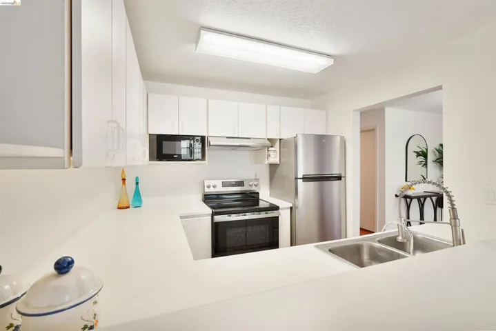Kitchen featuring white cabinetry, light countertops, stainless steel appliances, and a double basin sink with a gooseneck faucet