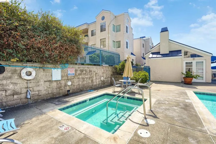 Outdoor spa and pool area with surrounding concrete decking, a stone retaining wall, and mature landscaping