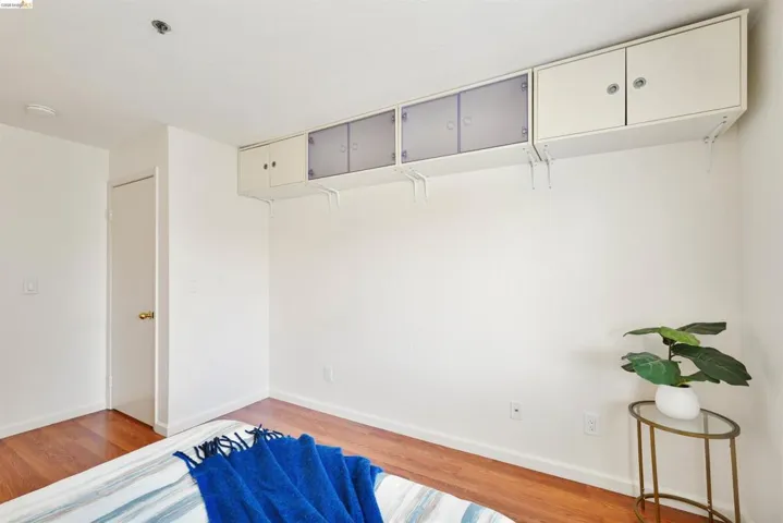 Room featuring wood-finish flooring, white walls, and built-in upper cabinetry with both solid and frosted panel doors