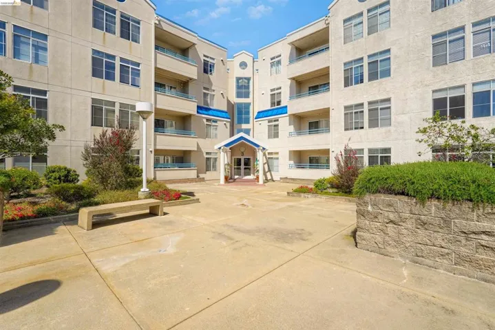 Multi-story building exterior with a stucco finish, individual balconies featuring blue railings, and a central entryway with a blue awning
