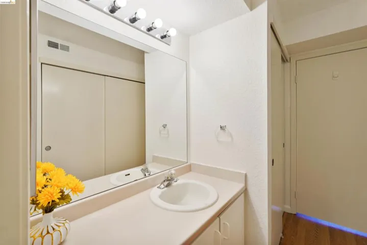 Bathroom vanity featuring an integrated sink, polished chrome faucet, and a large mirror with overhead vanity lighting