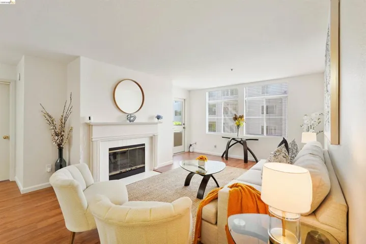 Bright living space featuring wood-finish flooring, a white mantel fireplace with a dark hearth, and multiple windows with horizontal blinds