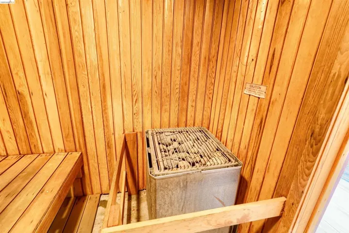 Private sauna featuring natural wood paneling, a built-in wood bench, and an electric sauna heater with rock capacity