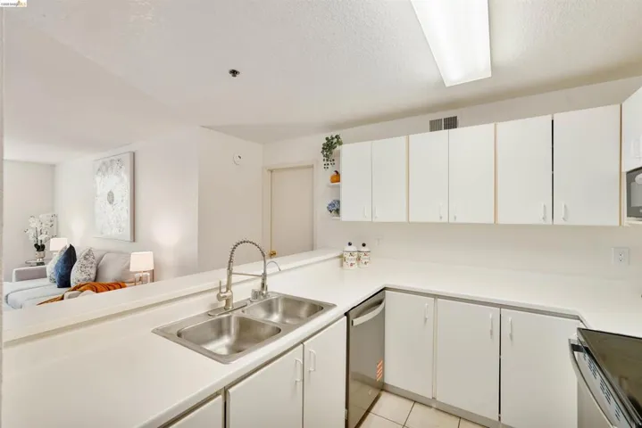 Kitchen featuring a double stainless steel sink with a high-arc faucet, white cabinetry, white countertops, and a stainless steel dishwasher