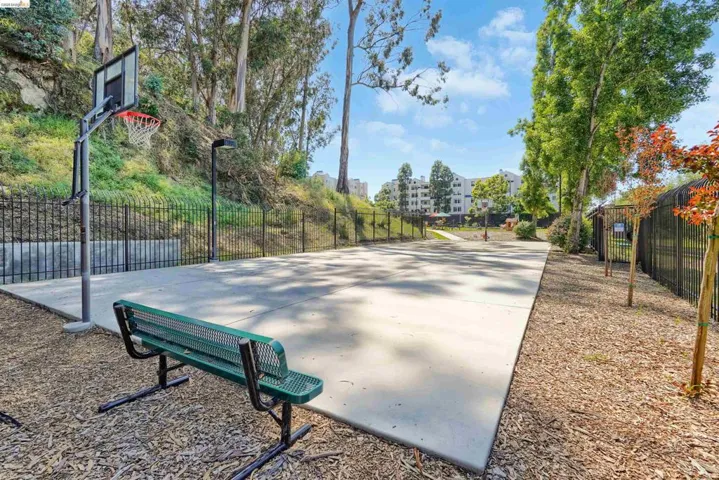 Concrete sports court with a basketball hoop and a green metal bench