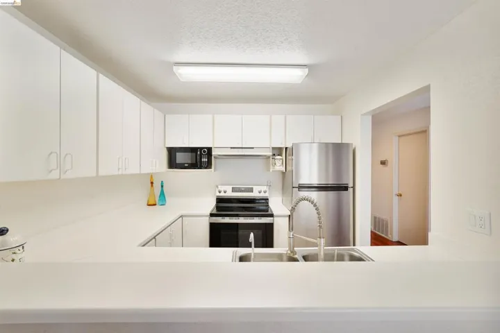 Bright kitchen featuring white cabinetry, a U-shaped countertop, stainless steel refrigerator, black microwave, and a double basin sink with a flexible faucet