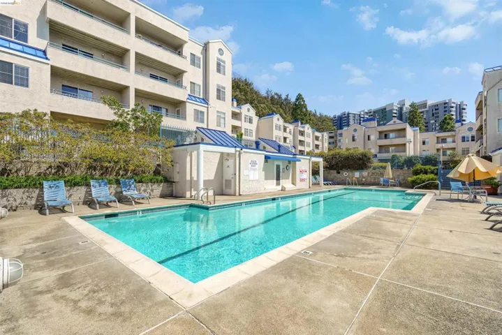 Rectangular swimming pool with concrete decking, surrounded by multi-story stucco buildings featuring blue-toned roofs