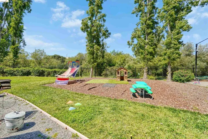 Expansive outdoor area featuring a dedicated play space with wood chips, a fenced perimeter, mature trees, and a manicured lawn